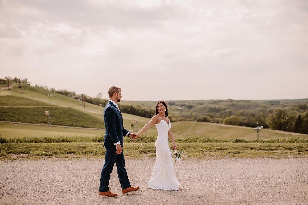 bride looking back at groom, walking down a road with ski hill in background