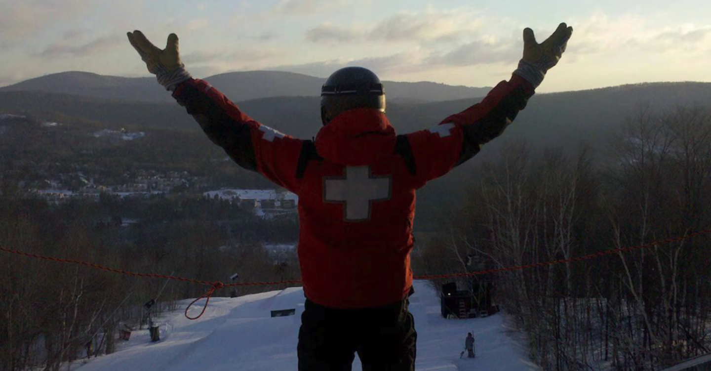 ski patroller looking over valley with arms up in excitement 