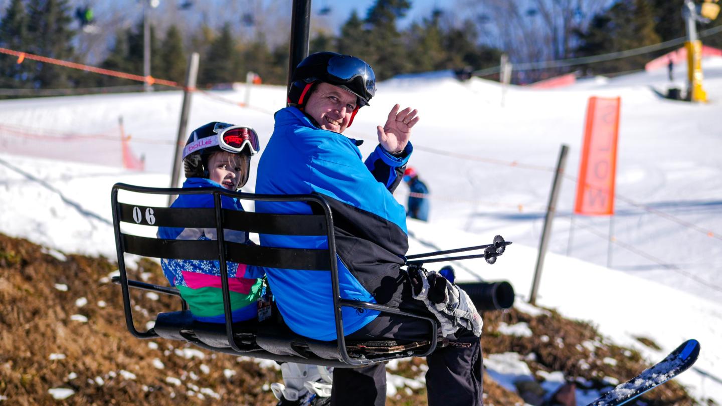 adult and child waving from chair lift