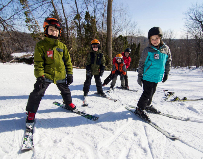 Group of kids smiling at camera with skis on