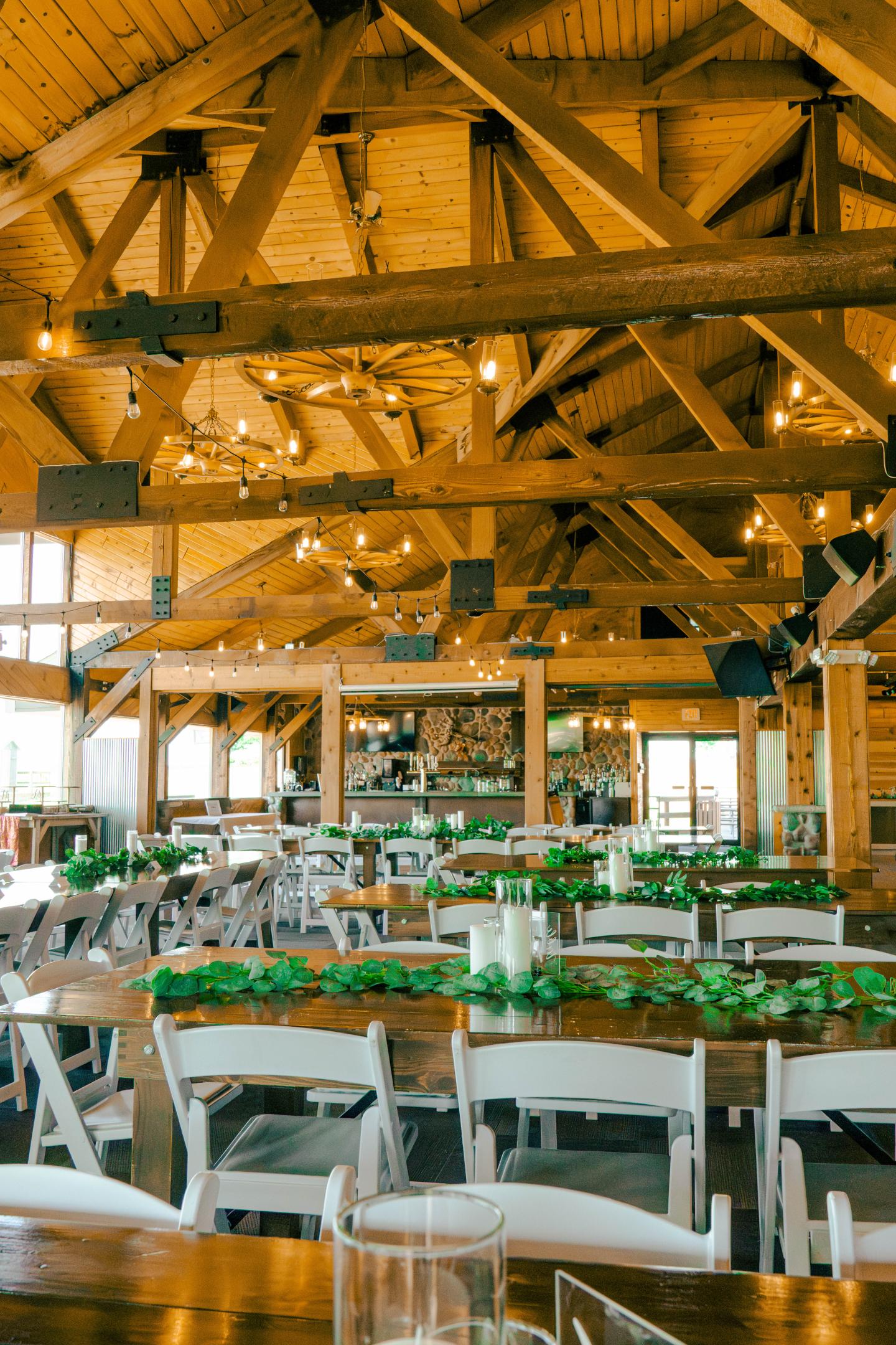Rustic dining hall with wooden beams, decorated tables, and white chairs.