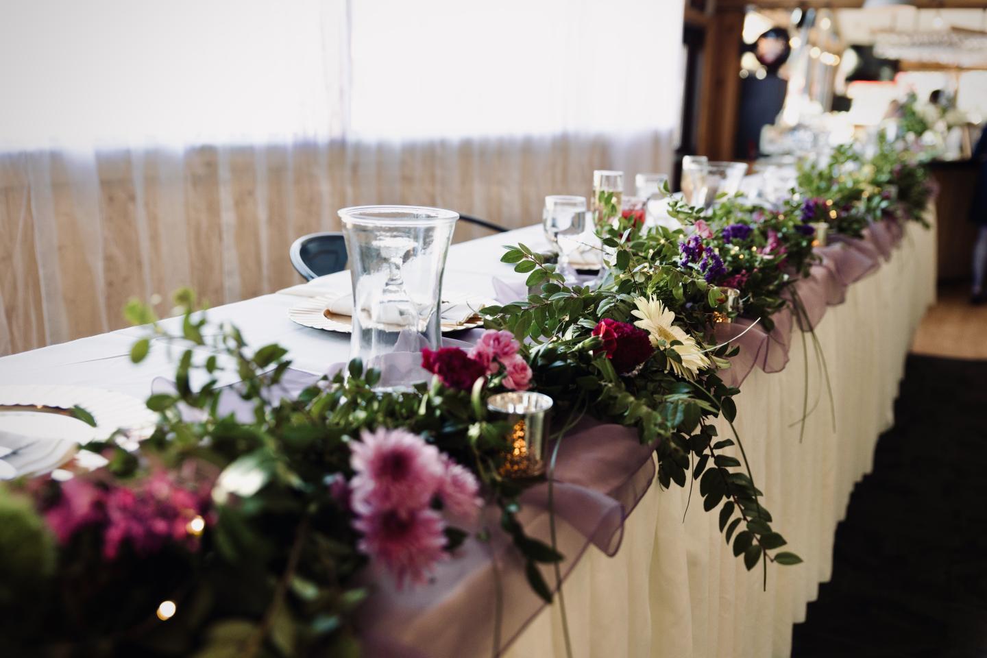 Elegant table with flower garland and candles under soft lighting.