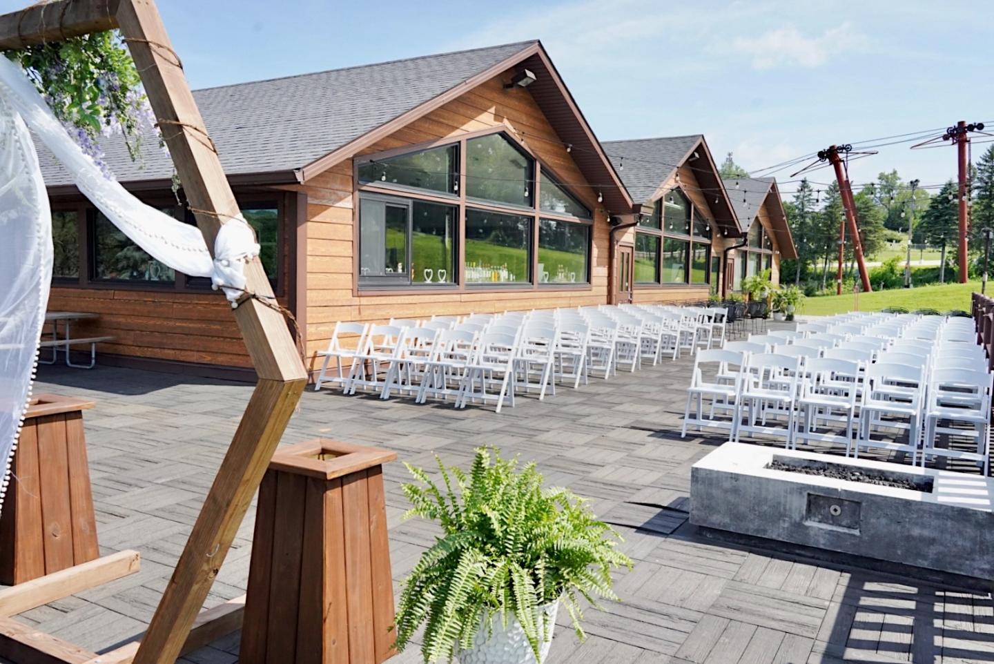 Outdoor wedding venue with chairs arranged and a wooden building in the background.