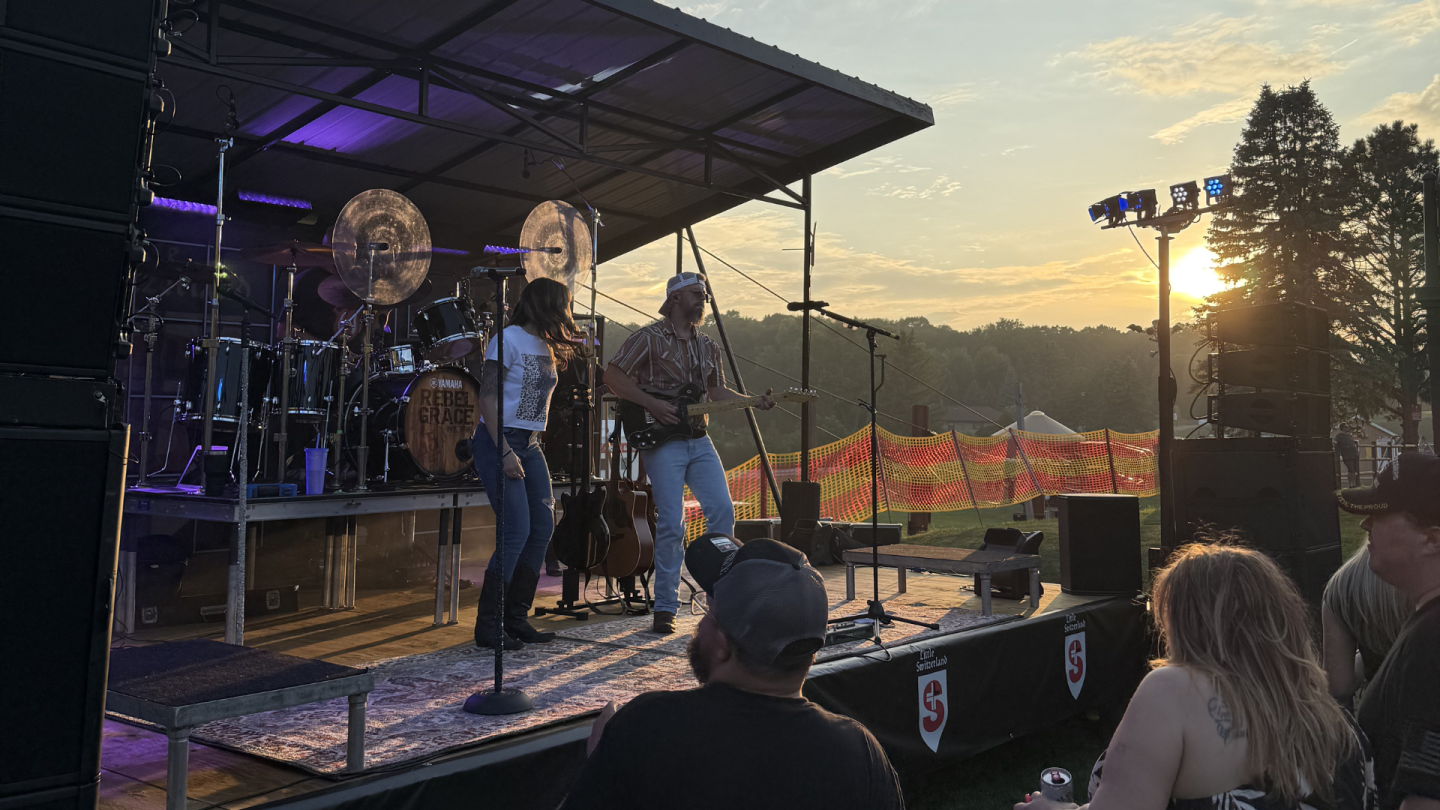 Band performing on outdoor stage at sunset, audience watching.