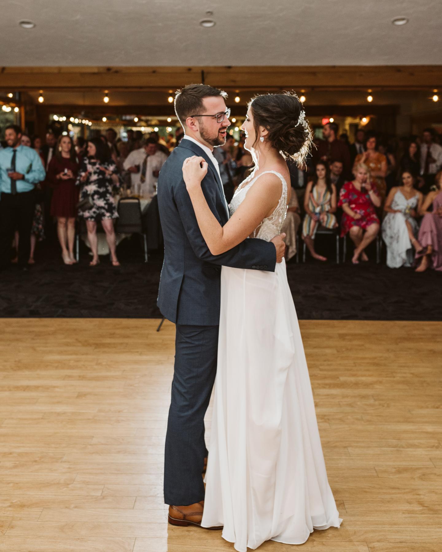 Couple dancing at a wedding reception, guests seated in the background.