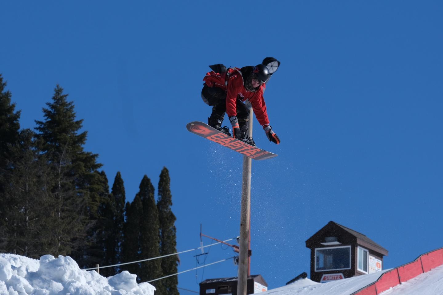 Snowboarder jumping off a snowbank against a clear blue sky.