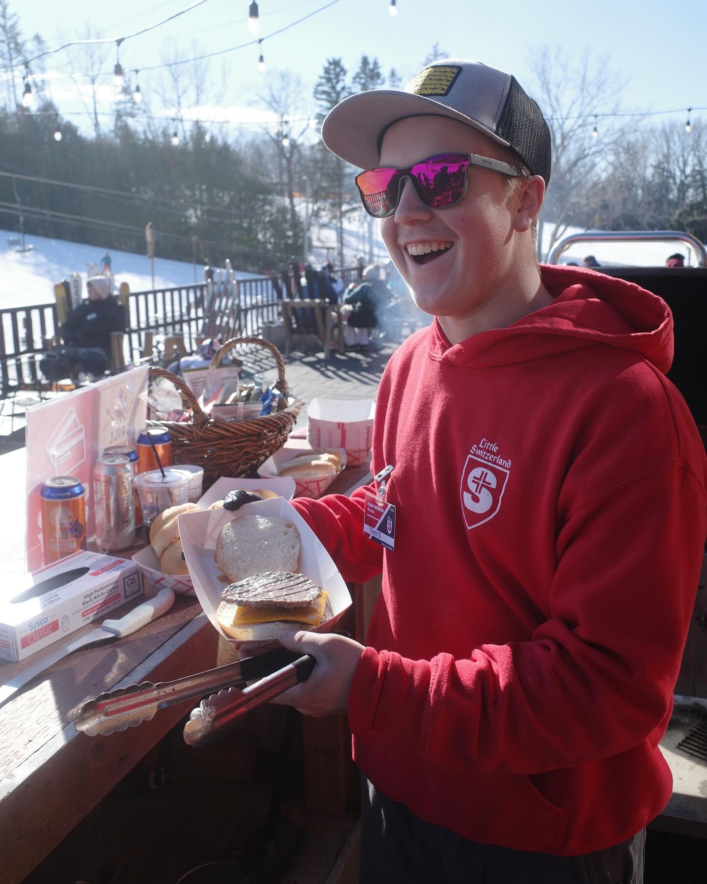 Smiling person in red hoodie with burger, outdoor setting, snowy background.