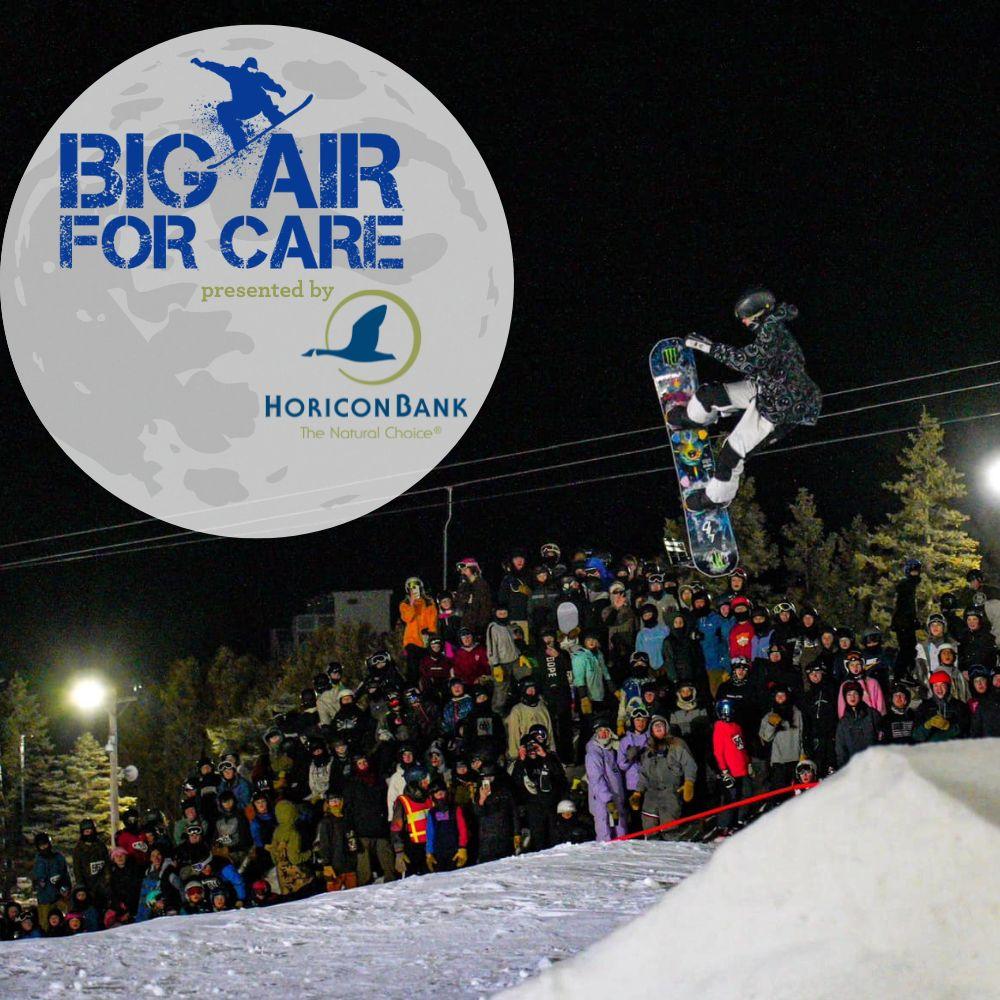 Snowboarder performing mid-air trick at night event, large crowd in the background.