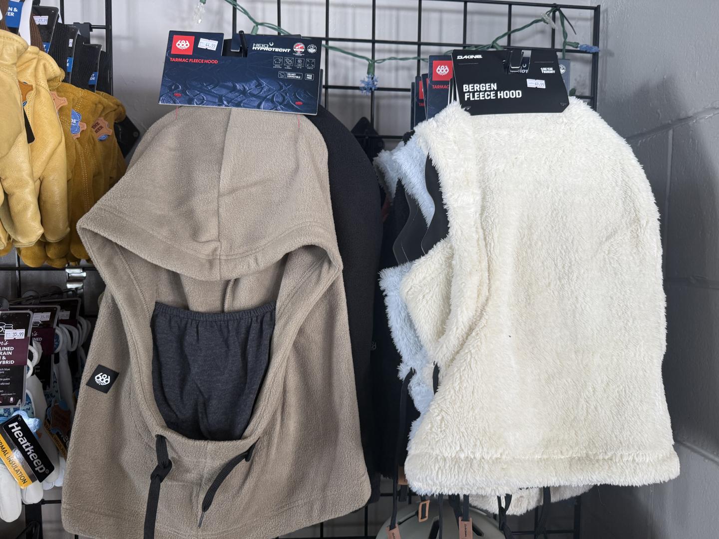 Tan hooded garment and white fleece vest on a display rack.