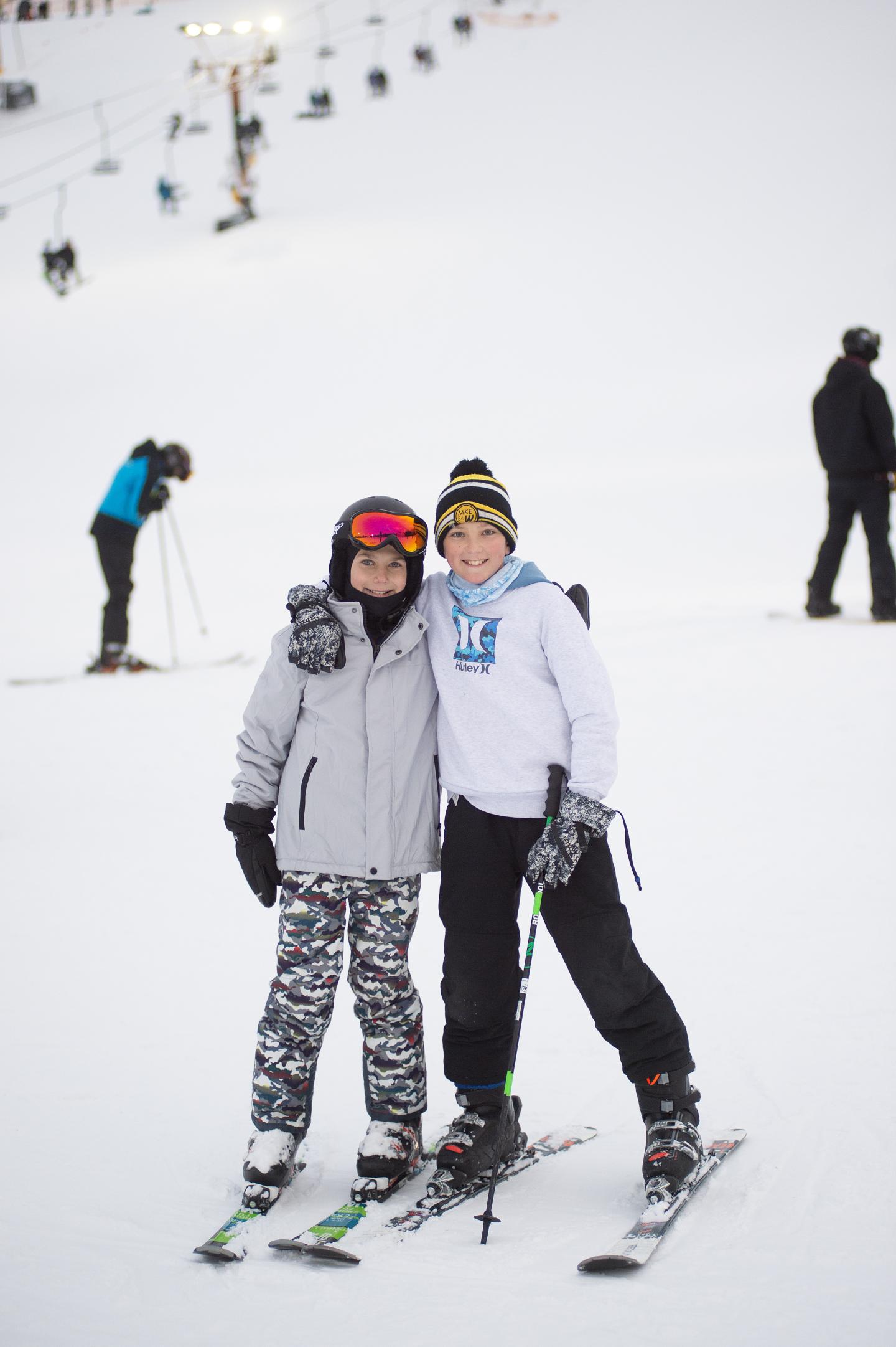 Two skiers smiling on a snowy slope, wearing winter gear.