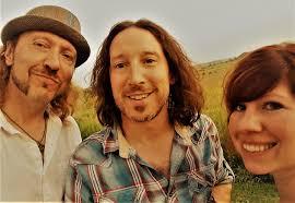 Three people smiling outdoors in a grassy field.