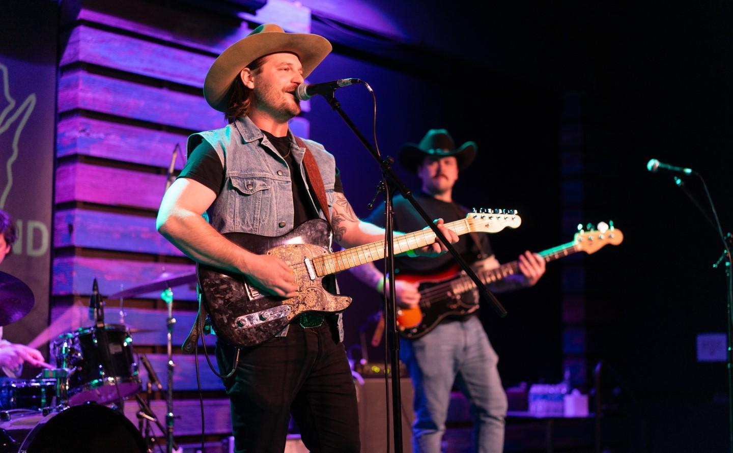 Band performing on stage, singer with cowboy hat playing guitar.