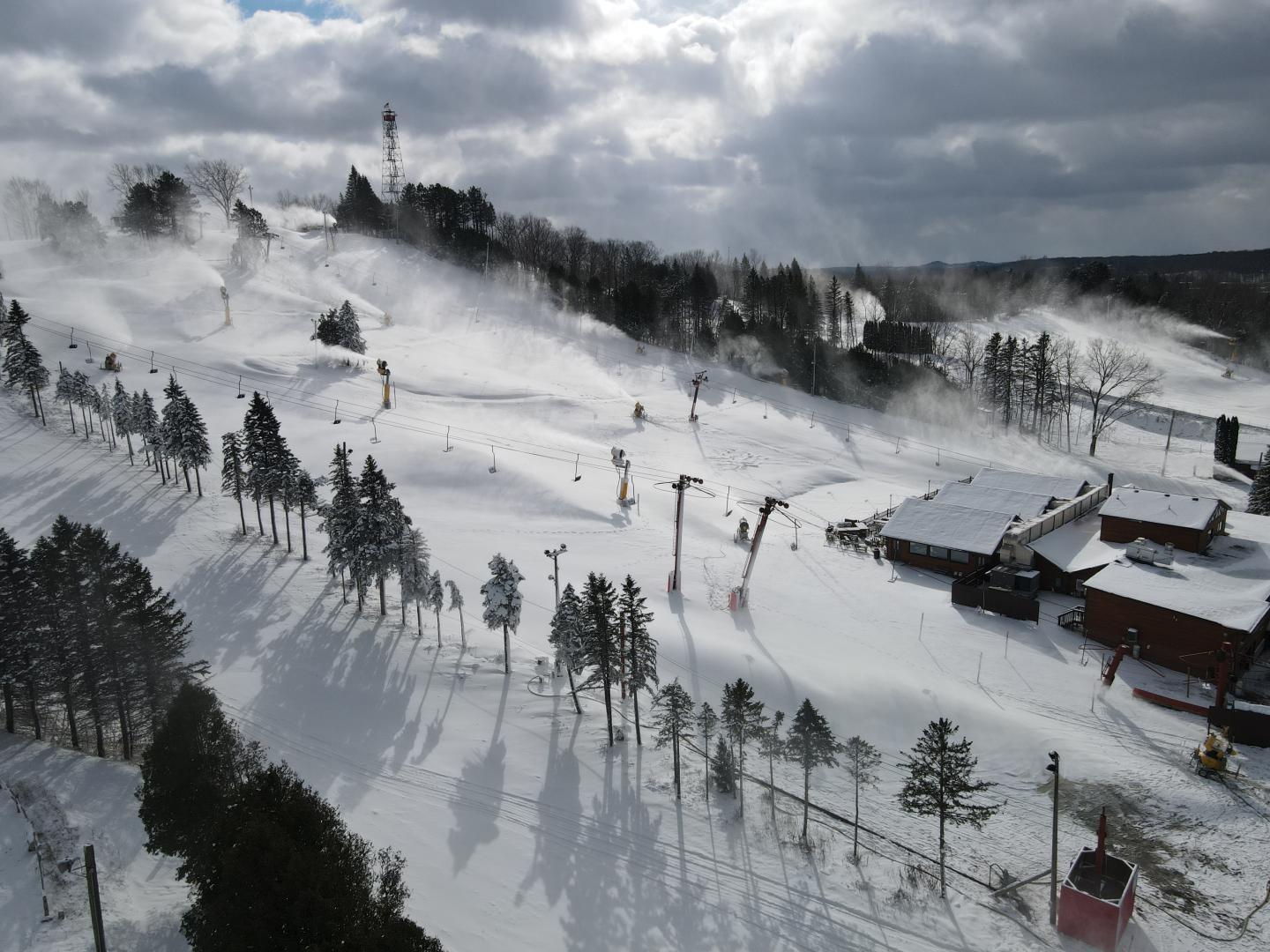 Snowy ski resort with ski lifts and cabins under cloudy skies.