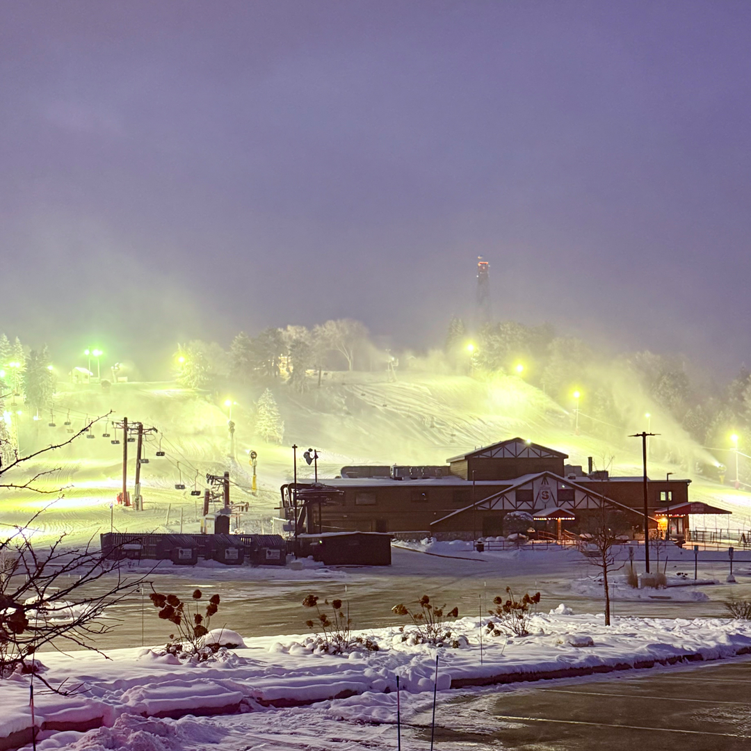Snowy ski resort at dusk with glowing lights on a slope.