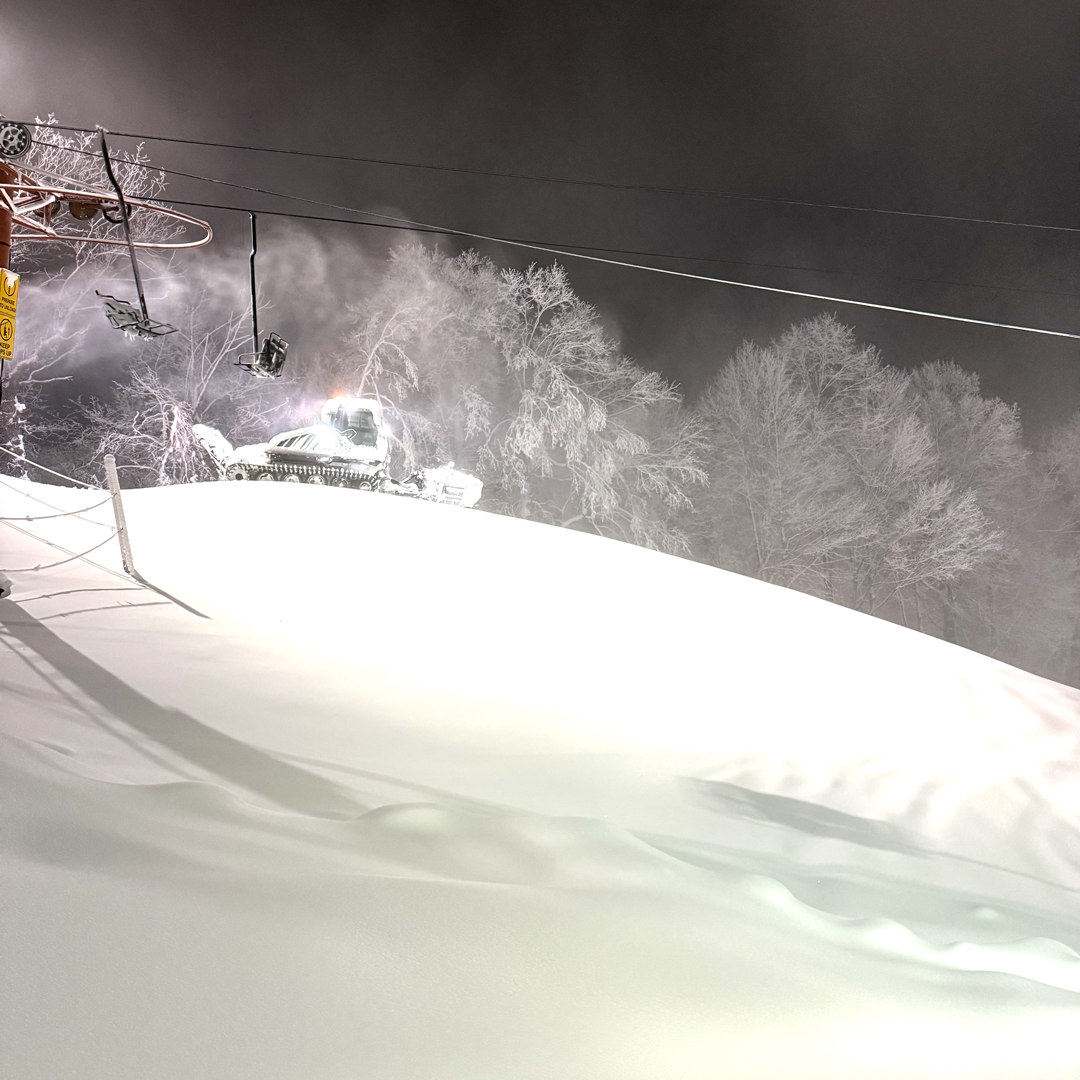 Snowy ski slope at night with a chairlift and snow-covered trees.