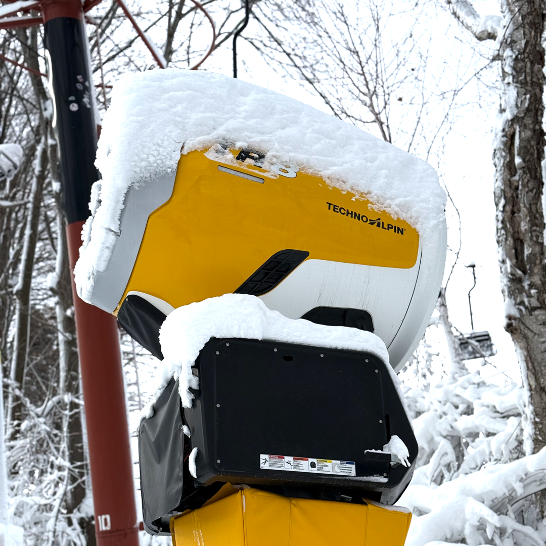 Yellow snow machine covered in snow, set in a snowy forest.