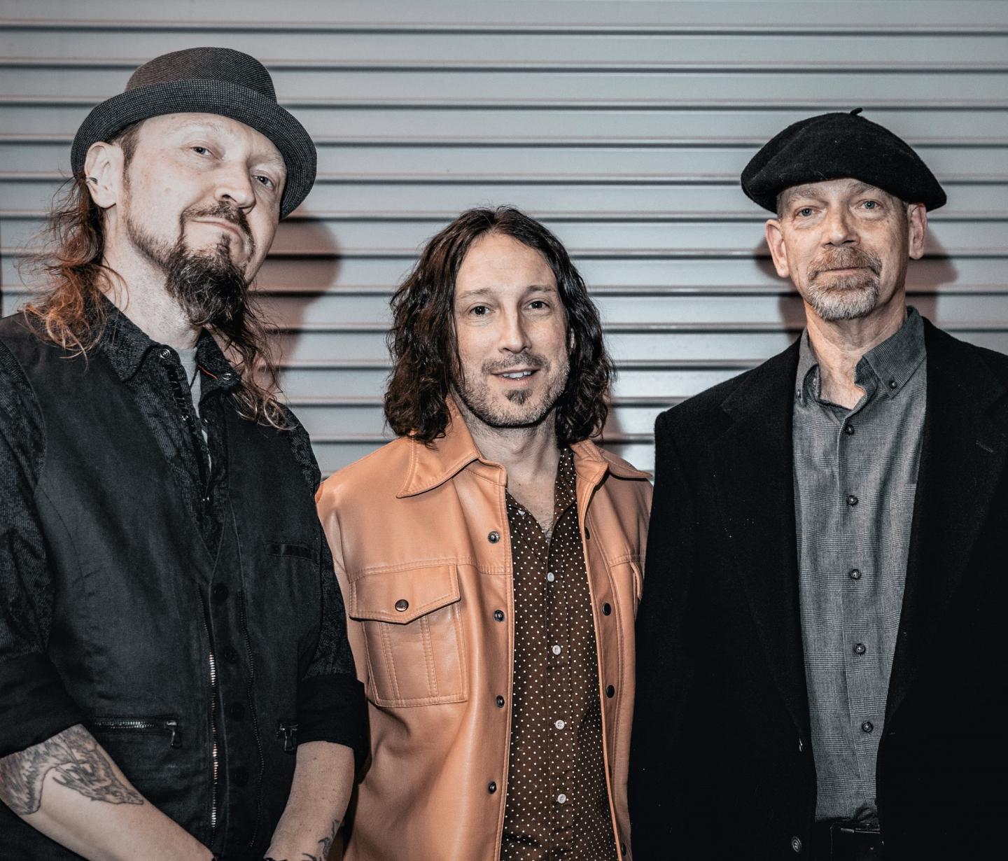 Three men standing together, smiling, wearing hats and casual jackets.