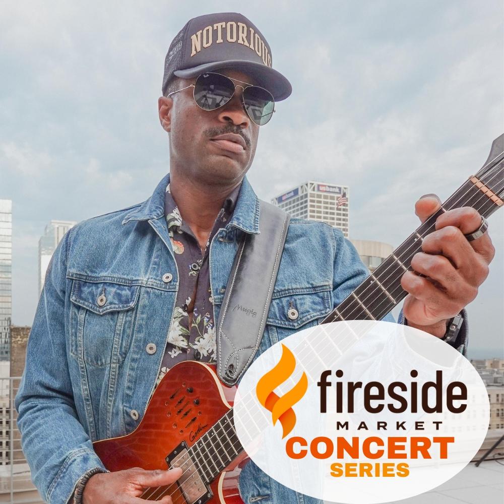Man in denim jacket and cap plays guitar outdoors; Fireside Market logo in corner.