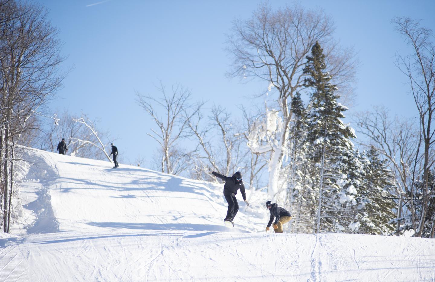 Skiers on a snowy hill under a clear blue sky.