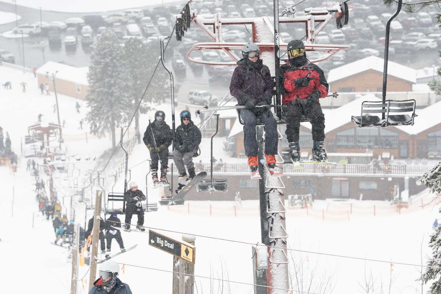 Skiers on a snowy chairlift, winter resort, overcast sky.