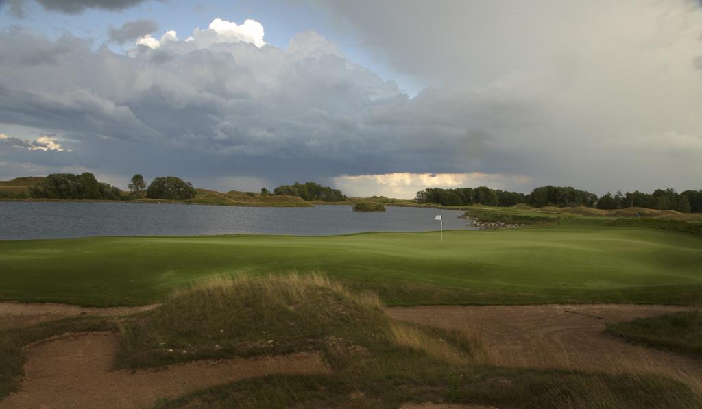 Golf course with a pond, under a cloudy sky.