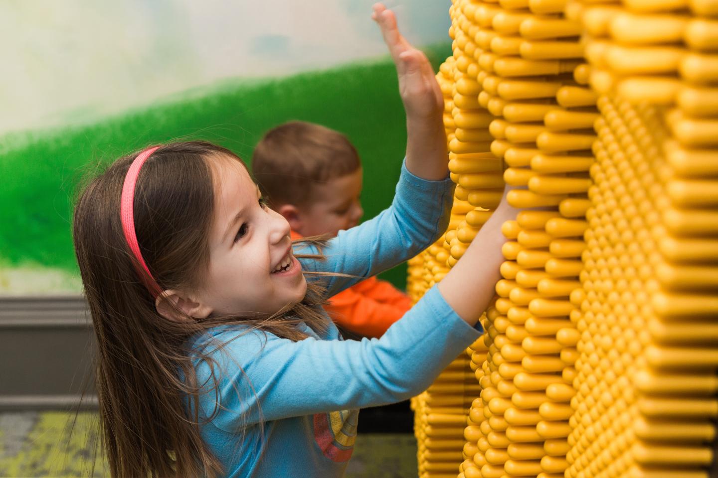 Young girl smiling, playing with large yellow interlocking blocks indoors.