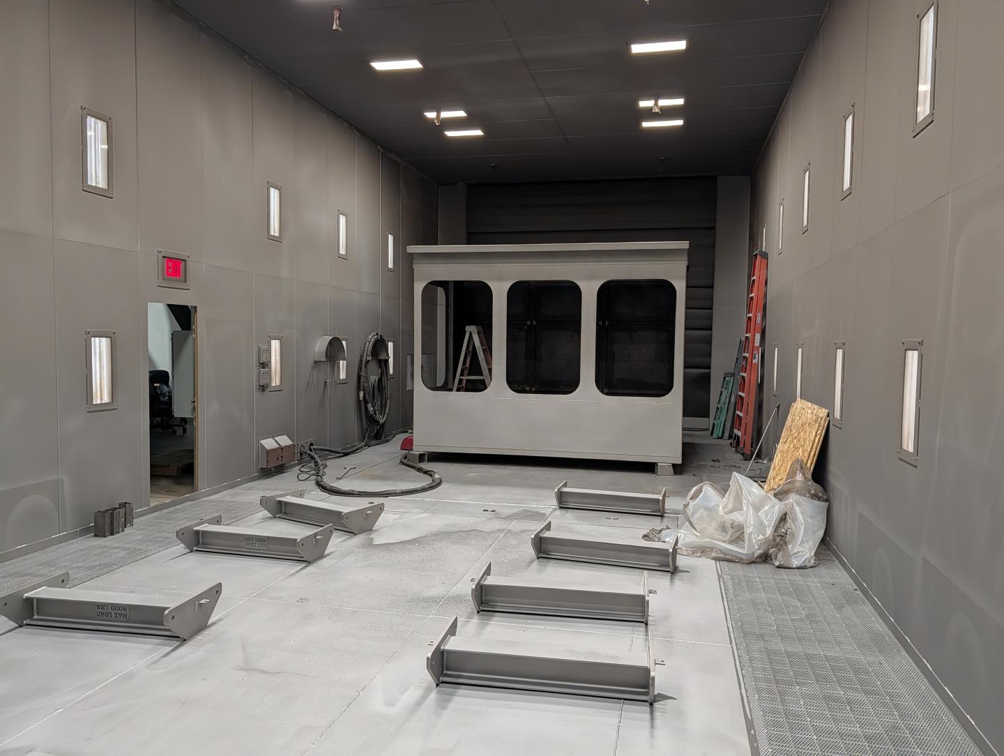 Industrial room with large equipment pieces on the floor, walls are gray, and lit by ceiling lights.