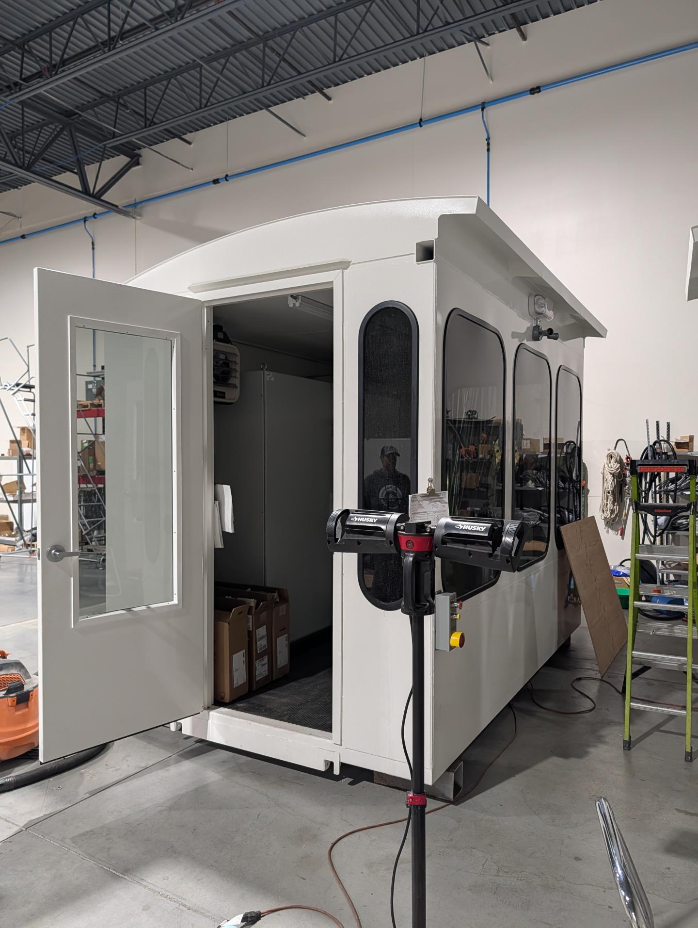 White modular room with glass doors in a warehouse setting.