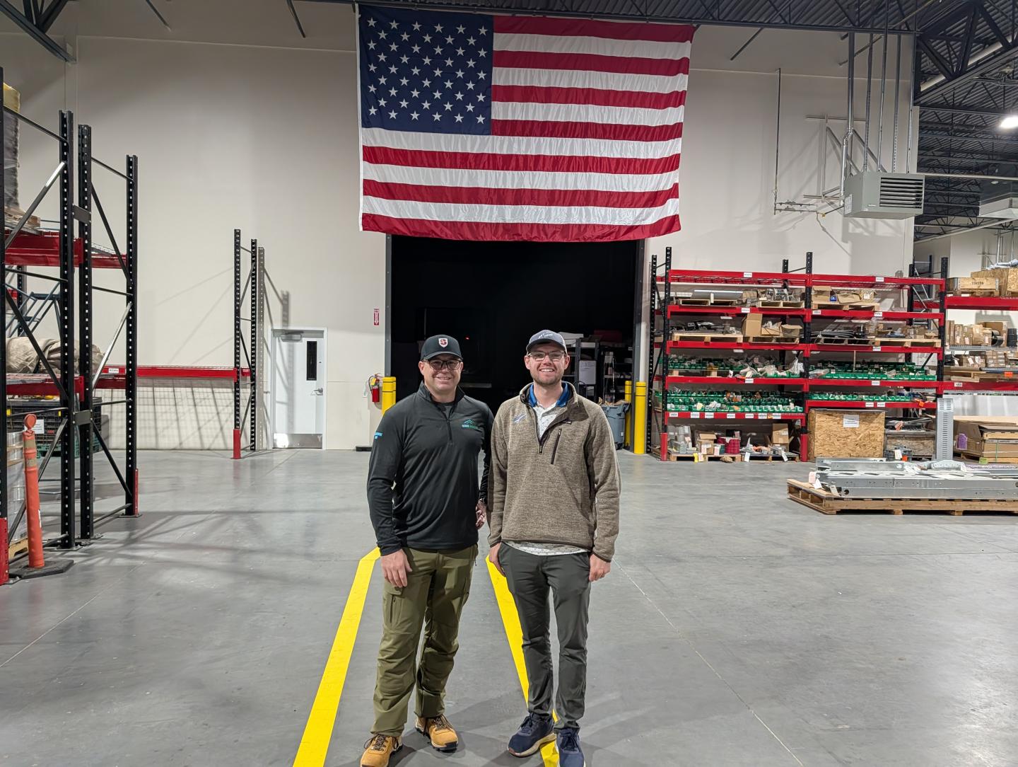 Two people standing in a warehouse under a large American flag.