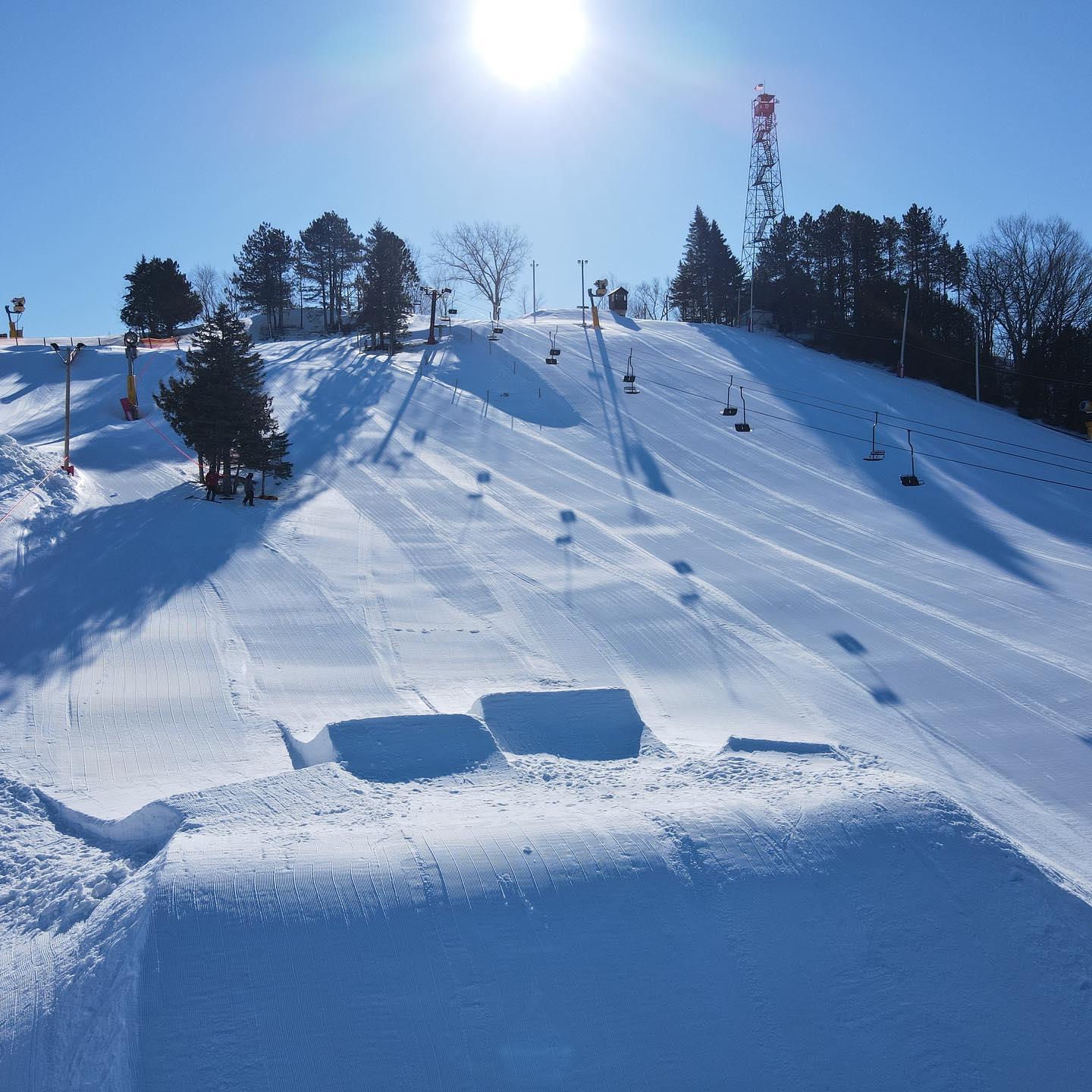 A snowy ski slope under a bright sun with a clear blue sky.