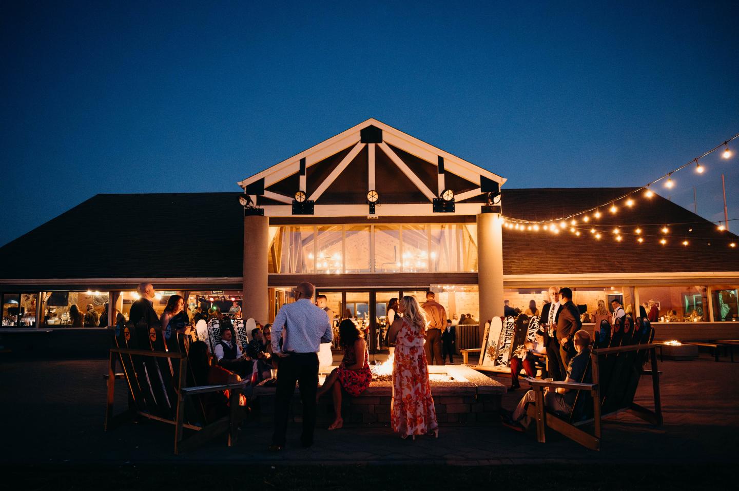 Outdoor evening gathering with people, lights, and a large building.