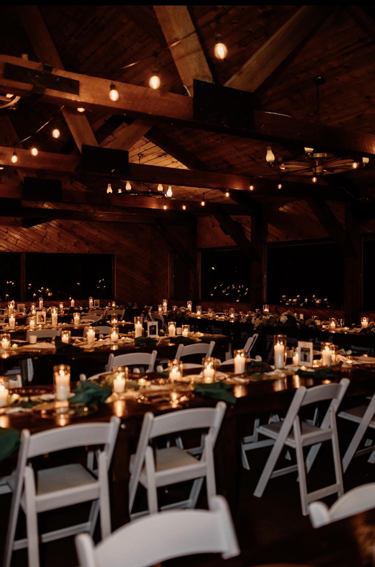 Dimly lit banquet hall with candles on tables and white chairs.