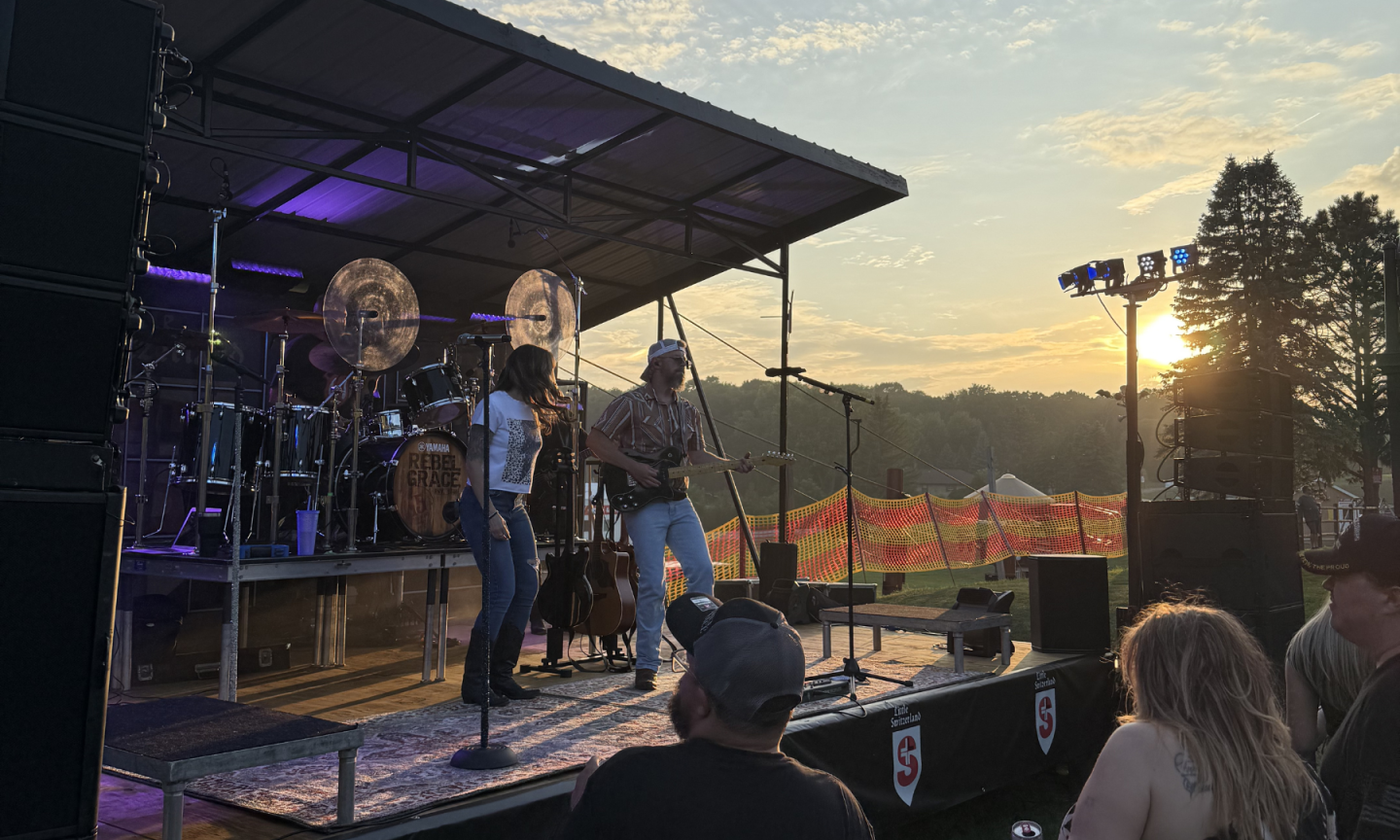 Band performing on an outdoor stage at sunset with an audience watching.