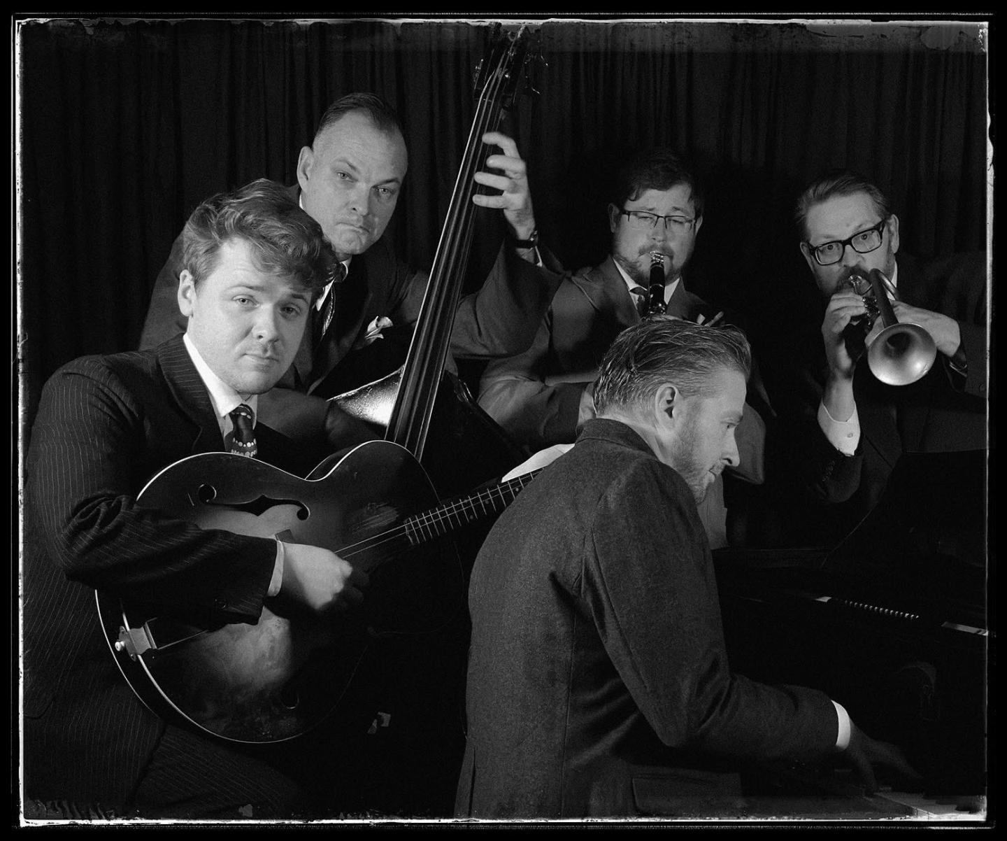 Jazz band performing with guitar, bass, piano, trumpet, and clarinet in black and white.