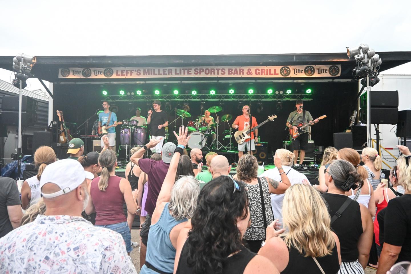 Outdoor concert with a band performing on stage, audience in foreground.