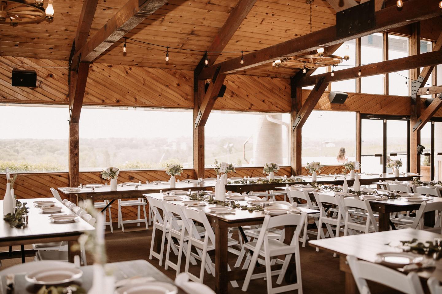 Rustic dining area with wooden beams and white chairs, set for an event.