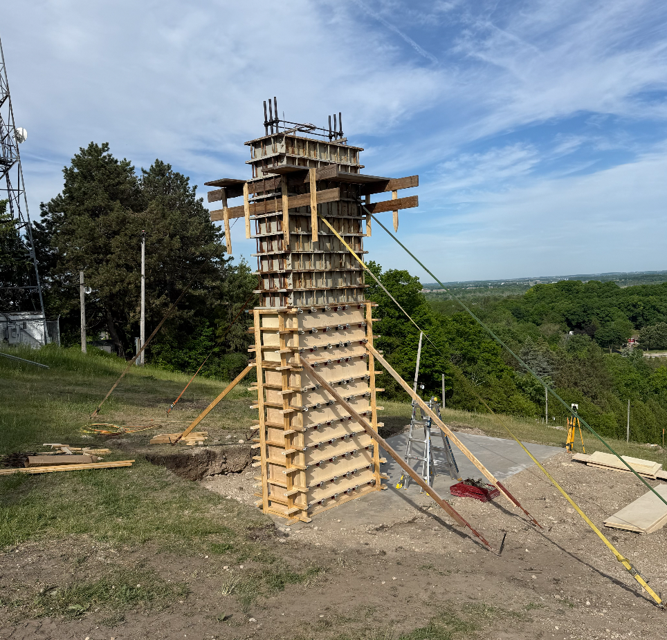 Wooden construction frame in grassy field under blue sky.