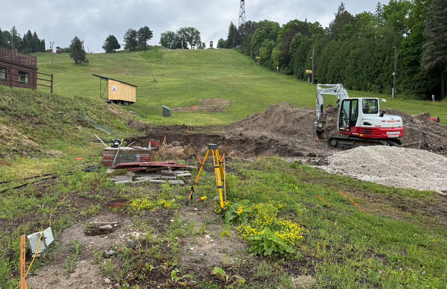 Grassy hillside with construction equipment and excavated soil, under a cloudy sky.
