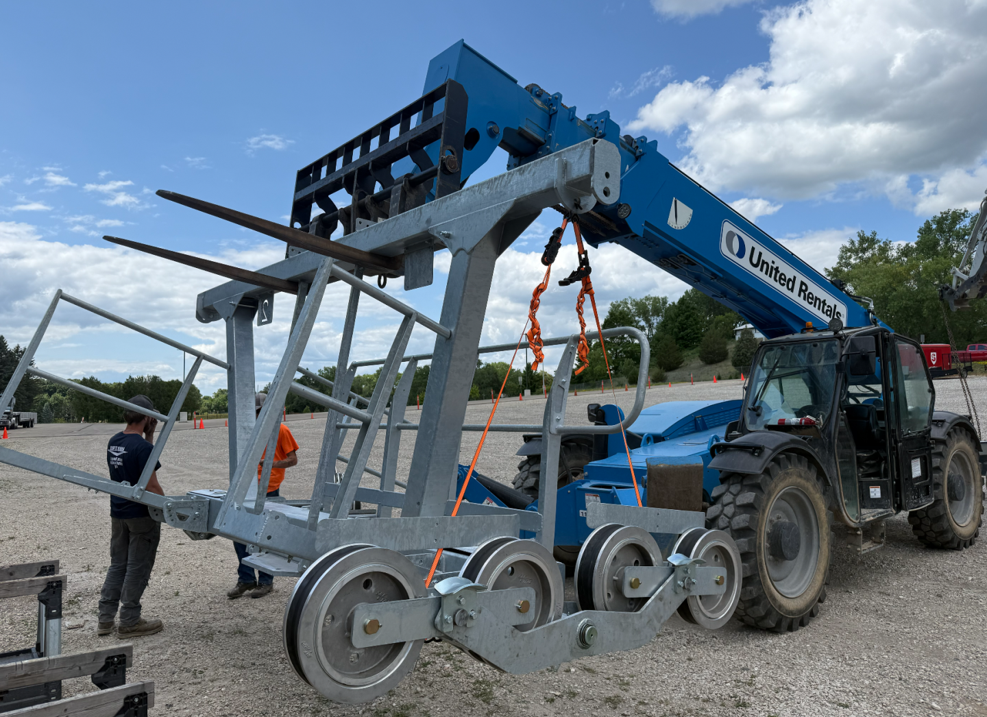 Blue forklift lifting a large metal frame with three workers around it.