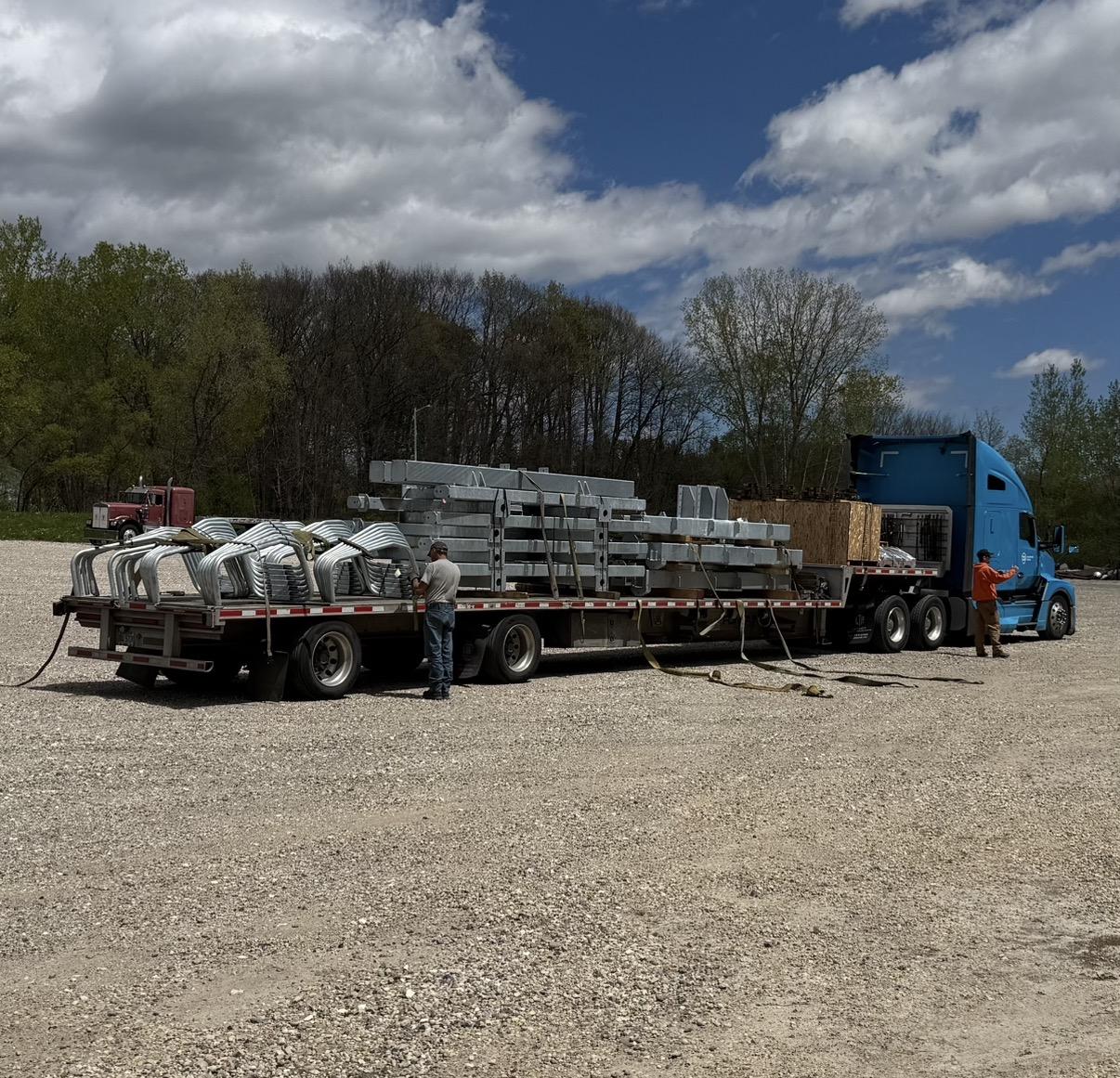 A large flatbed truck with cargo in a gravel lot under a cloudy sky.