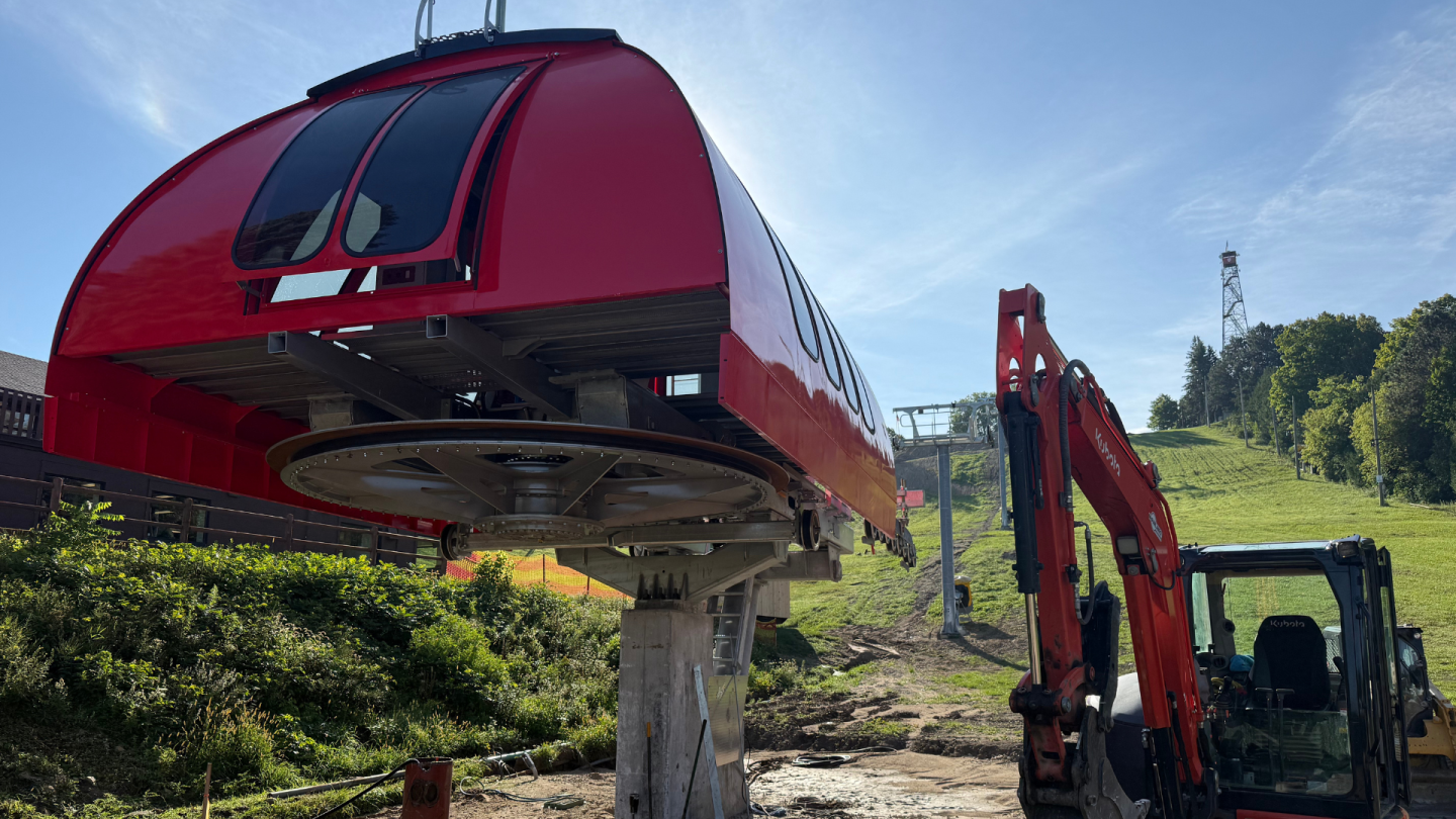 Red cable car cabin lifted by crane in a grassy mountain field.