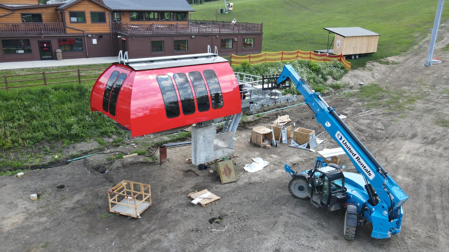 Red cable car installation near a lodge, with a blue crane and grassy terrain.