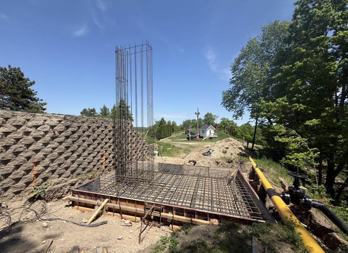 Construction site with rebar, dirt mounds, and trees under a clear sky.