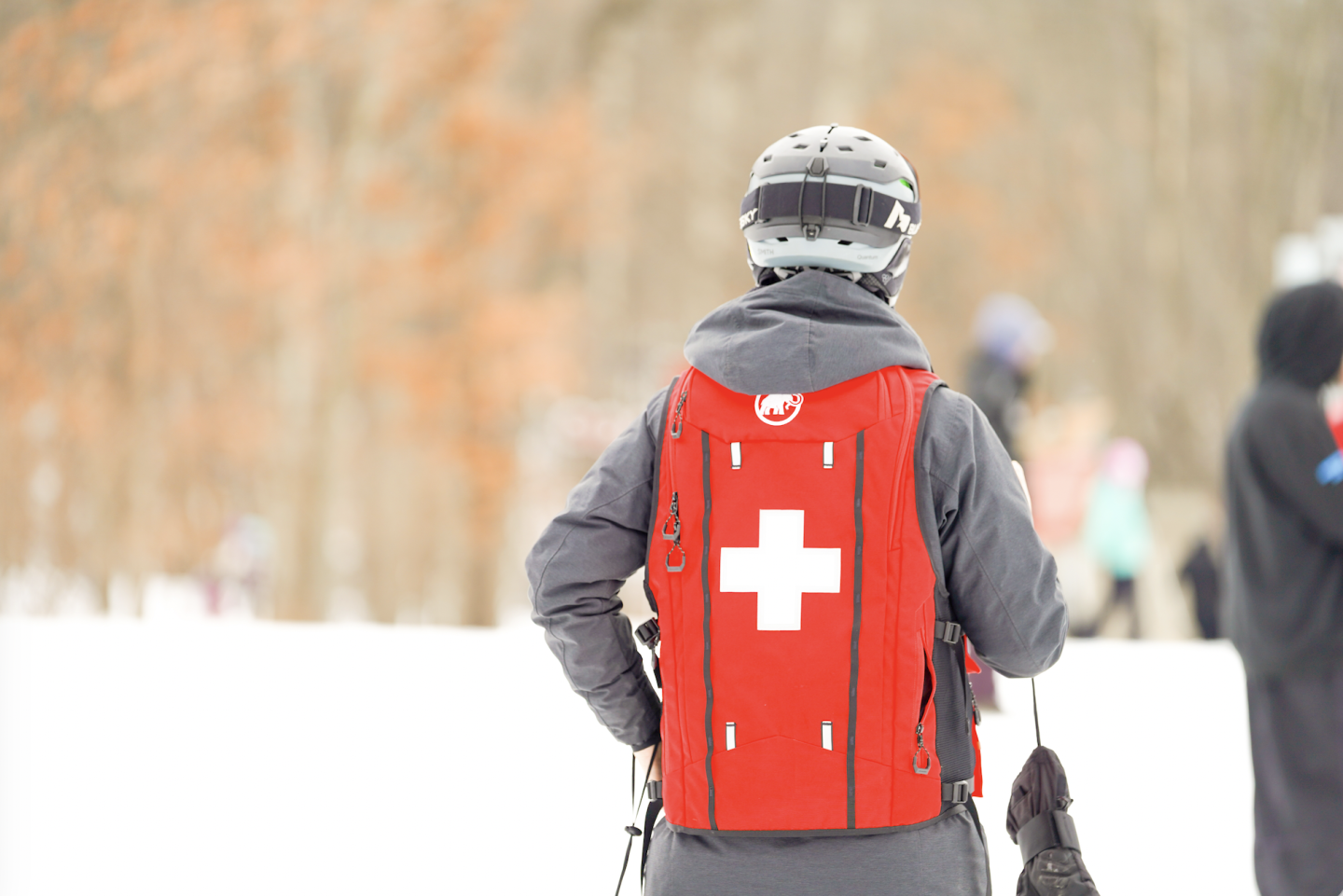 Ski patrol member in red vest with a white cross, snowy background.