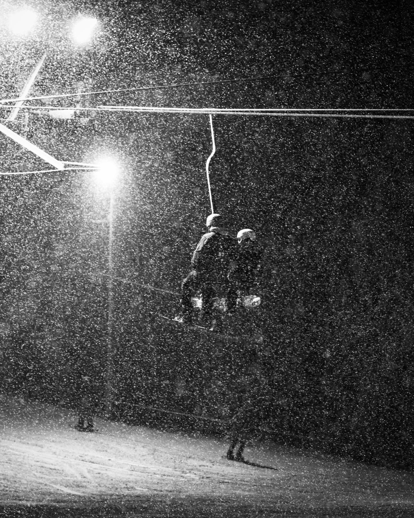 Grainy black-and-white photo of a skier jumping beneath a streetlight at night.