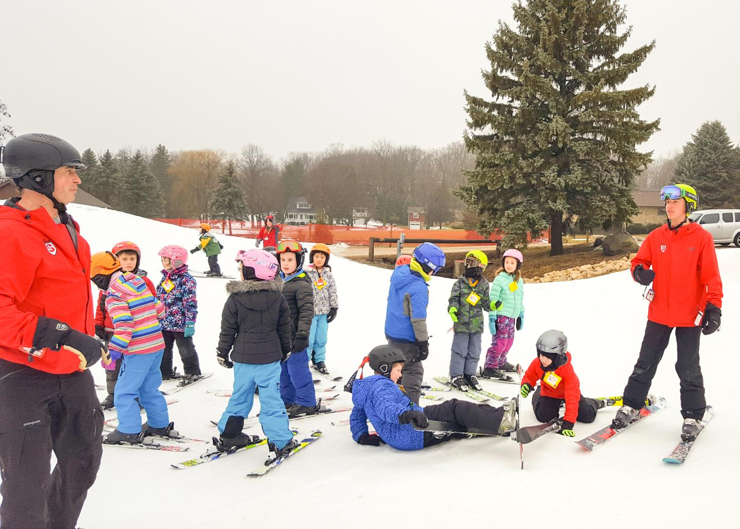 Children in colorful ski gear gather on snow with instructors.