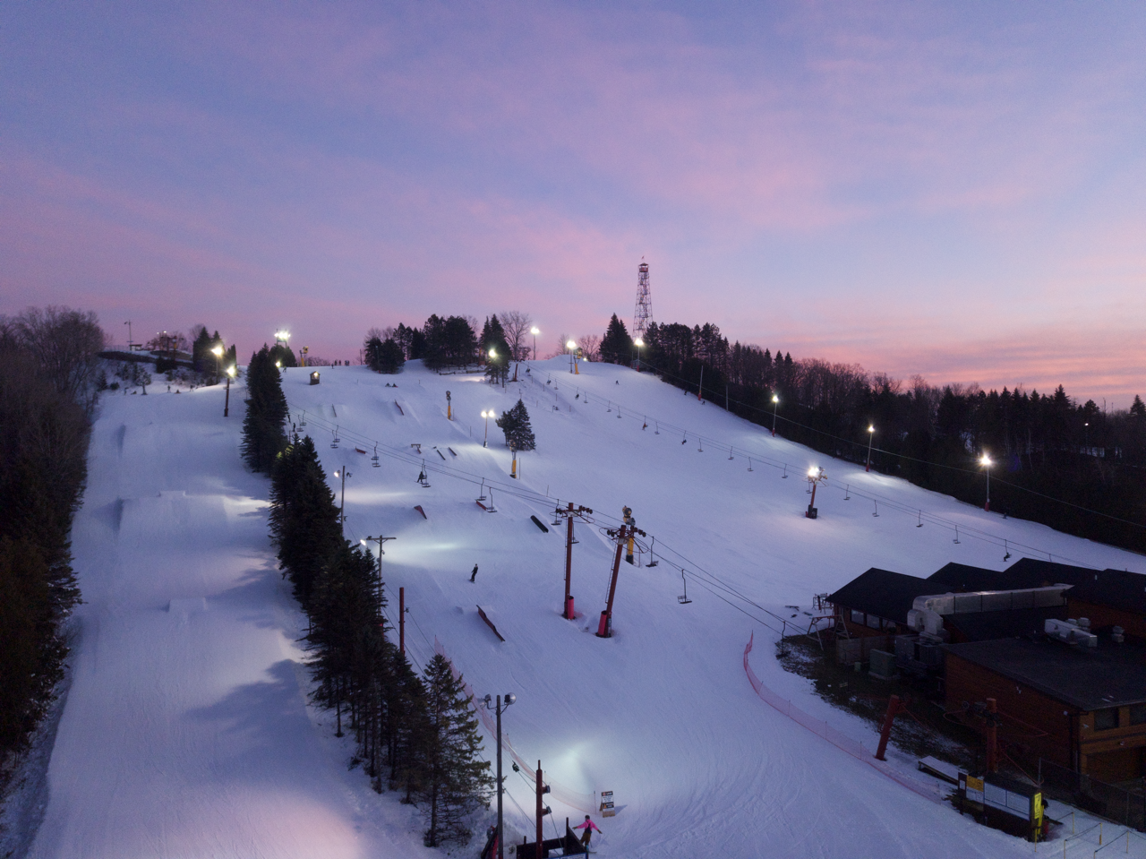 Dusk view of a snow-covered ski slope with skiers and chairlifts.