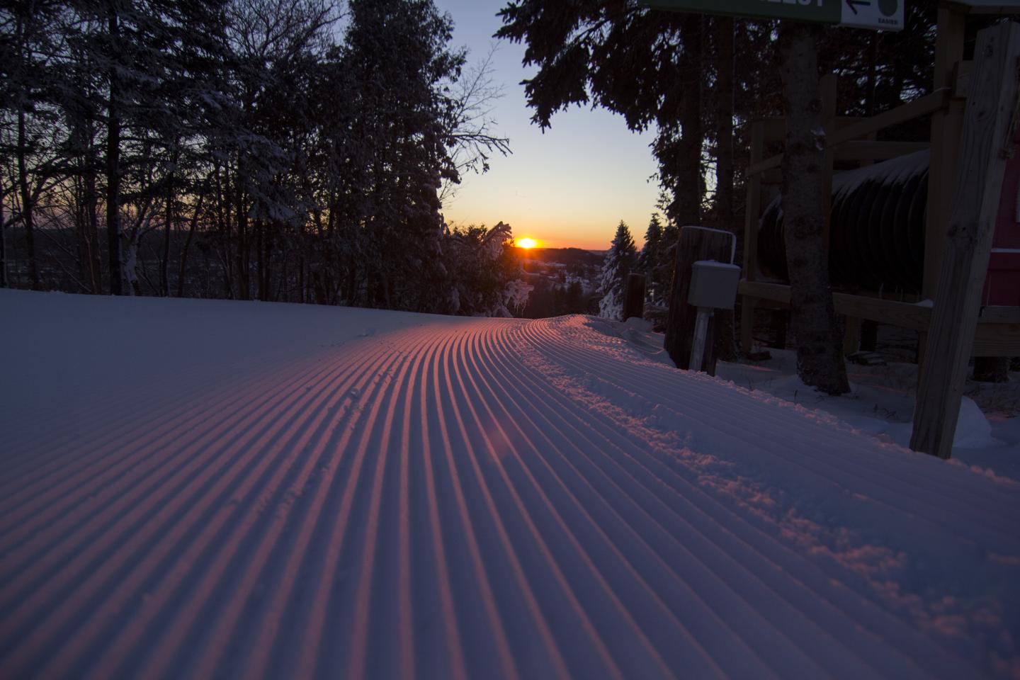 Sunset over a freshly groomed snowy trail through dark trees