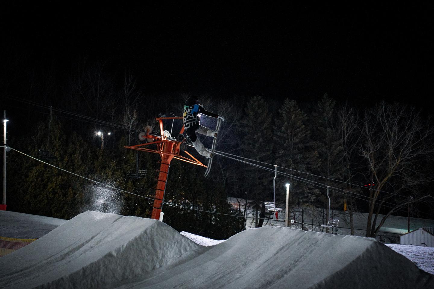 Nighttime ski slope with a chairlift passing above snow-covered jumps.