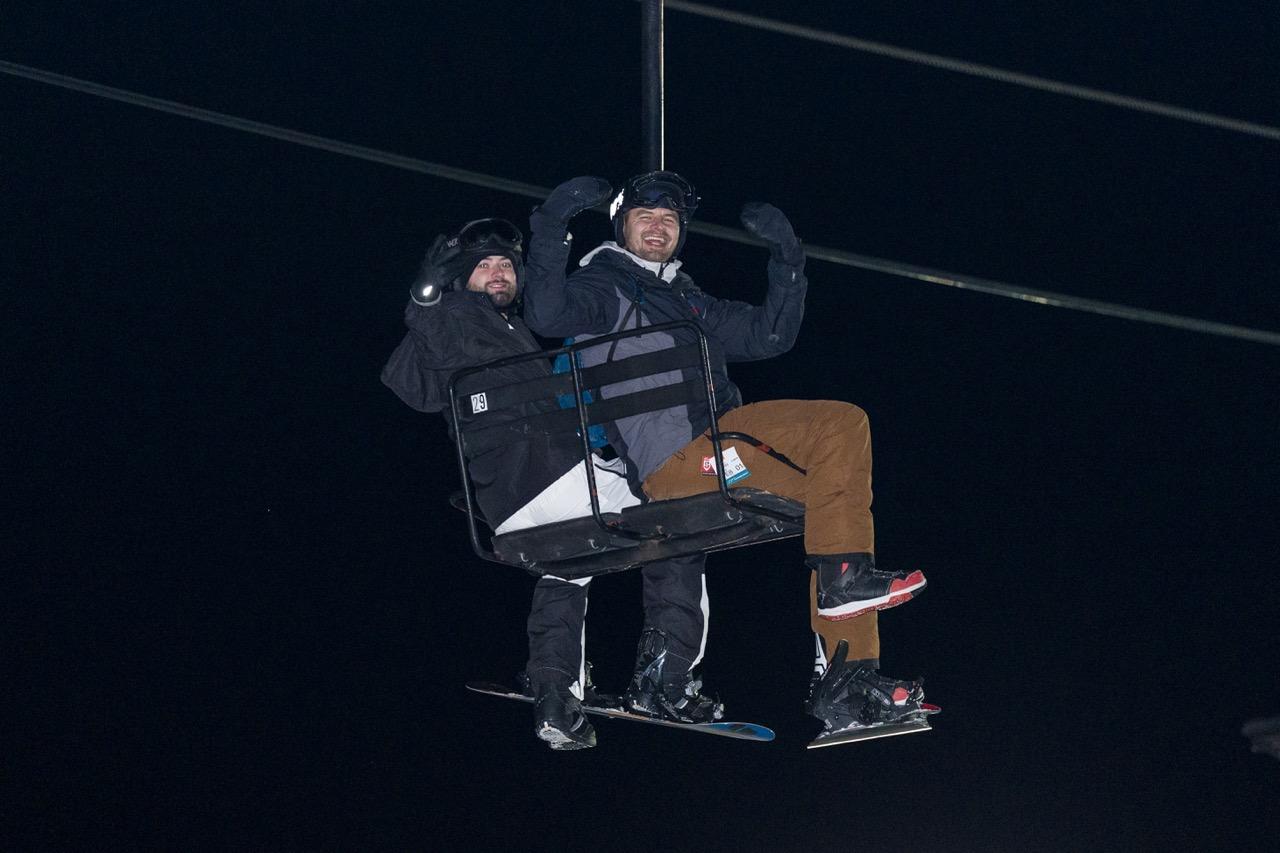 Two bundled-up skiers riding a chairlift at night